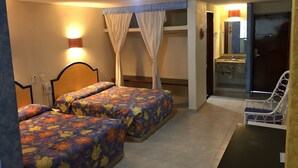 Una habitación de hotel con dos camas, un baño con espejo y una silla.