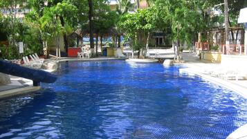 A swimming pool with clear blue water, surrounded by trees and lounge chairs.
