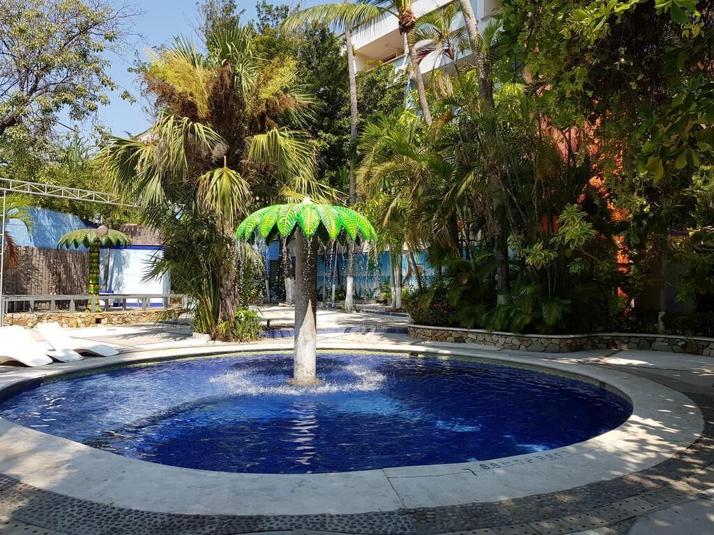 A circular pool with a central fountain, surrounded by palm trees and a stone pathway.