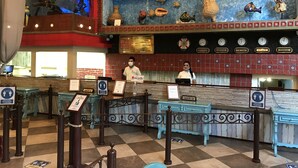 Un vestíbulo de hotel con mostrador de recepción, un reloj que muestra diferentes zonas horarias y una pared decorada con peces y conchas.
