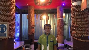 Una zona de bar con un cantinero, botellas de Corona Extra y diversas bebidas en la barra.