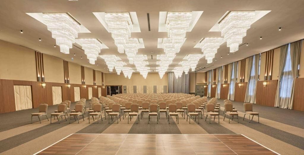 Un salón de conferencias con hileras de sillas, una lámpara de araña grande y suelo de madera.