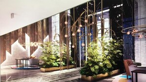 Een moderne lobby met een marmeren vloer, potplanten, een zithoek en een decoratieve wand met verticale lijnen.