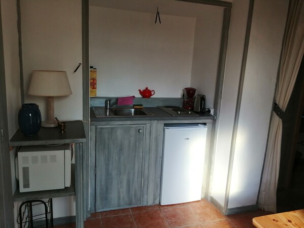 Una cocina compacta con un lavamanos, una cafetera y un refrigerador pequeño.