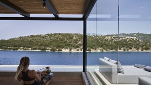 A modern room with a view of a body of water and hills, a rowing machine, and a sofa with cushions.