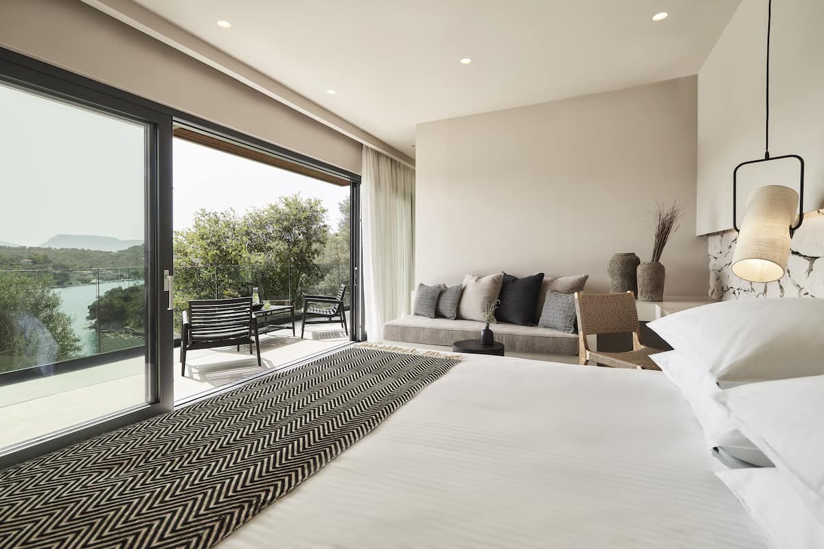 Ett modernt hotellrum med en stor säng, en soffa, en fåtölj och utsikt över en sjö.