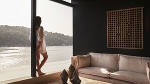 A room with a large window overlooking a body of water, a beige sofa, and a decorative screen.