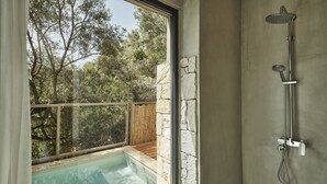 A bathroom with a shower, a window overlooking a pool, and a stone wall.