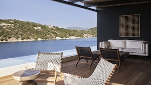 A balcony with wicker chairs, a white sofa, and a view of a body of water and hills.
