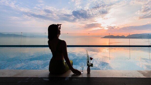A person sitting by a pool with a sunset view. - Grand Gosia Hotel (Nha Trang)