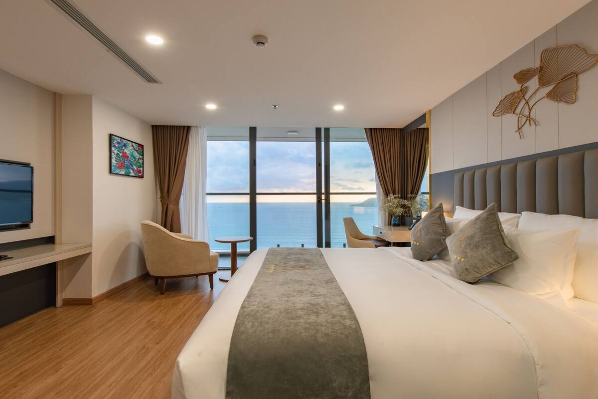 Een moderne hotelkamer met een groot bed, een televisie, een bureau en uitzicht op zee.
