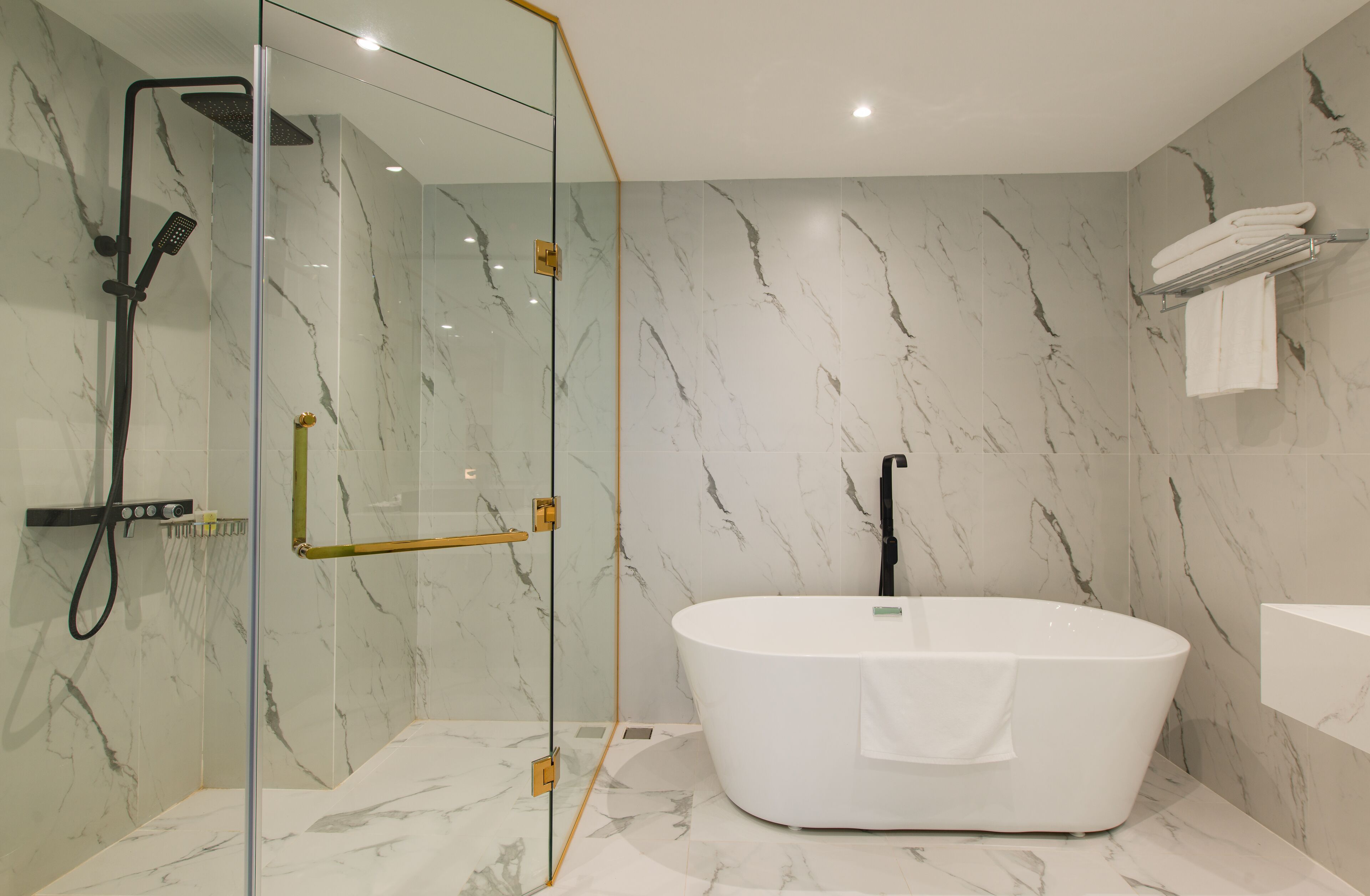 A modern bathroom with a glass-enclosed shower, a freestanding bathtub, and marble walls.