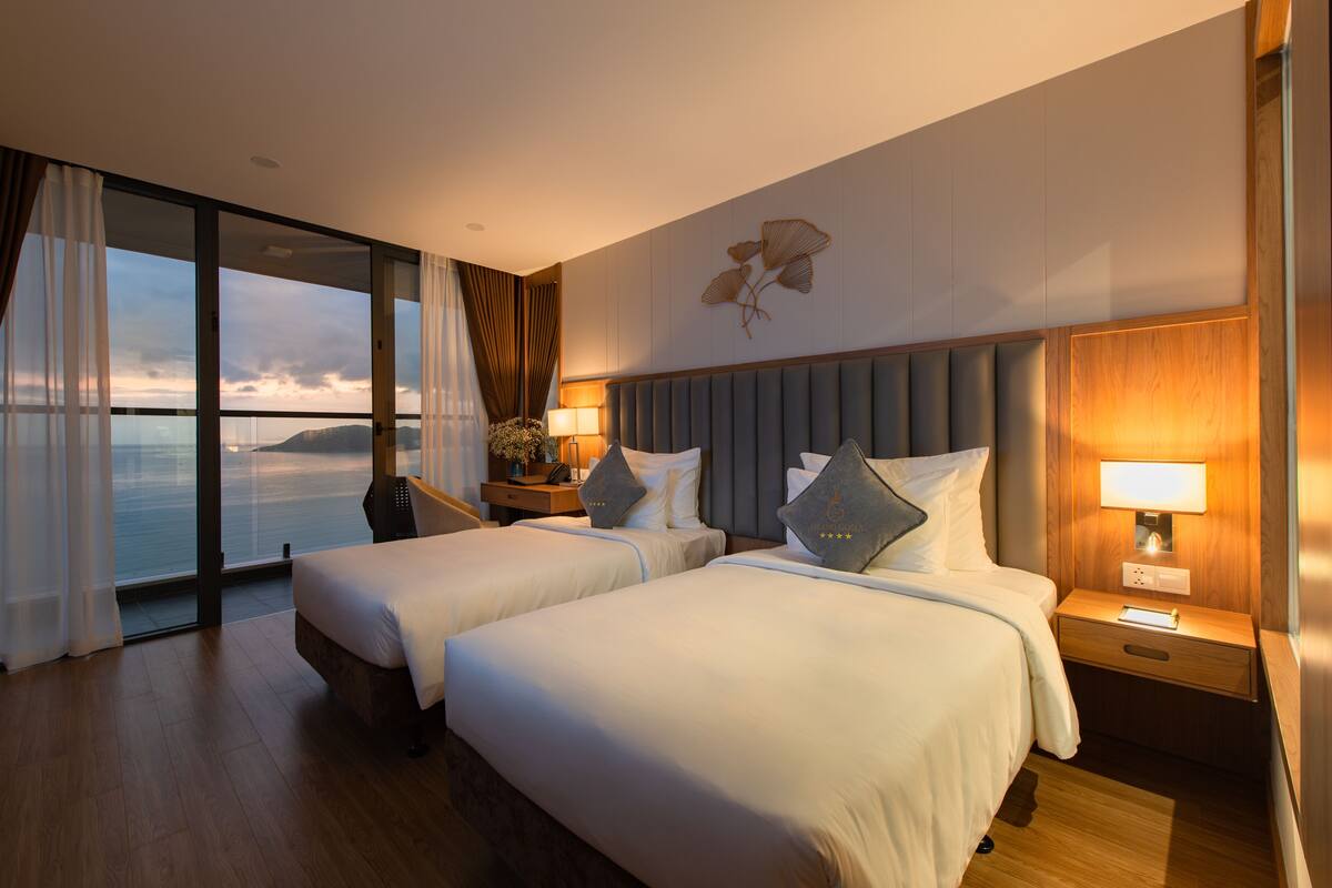Een hotelkamer met twee bedden, een groot raam met gordijnen, een nachtkastje met een lamp en een wandlamp.