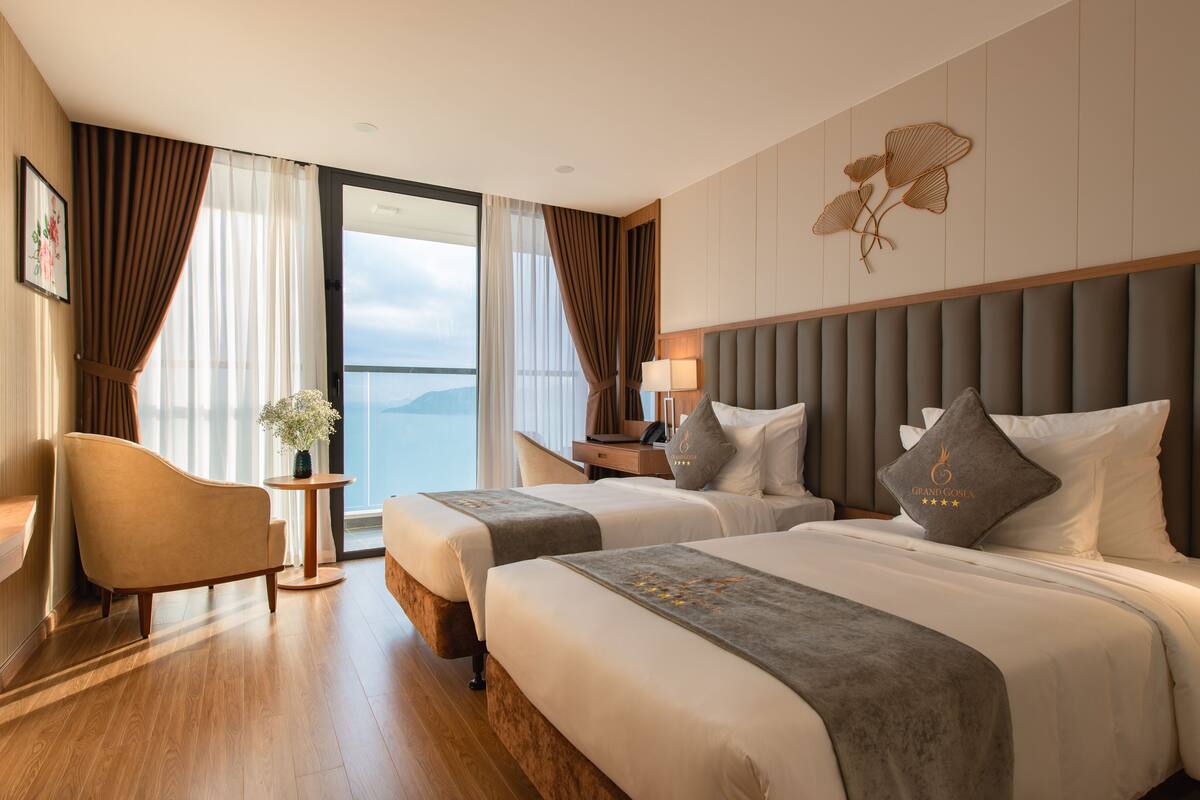 Een hotelkamer met twee bedden, een zithoek en uitzicht op zee.