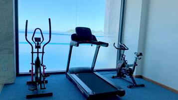 A gym with a treadmill, elliptical, and stationary bike, overlooking a body of water.