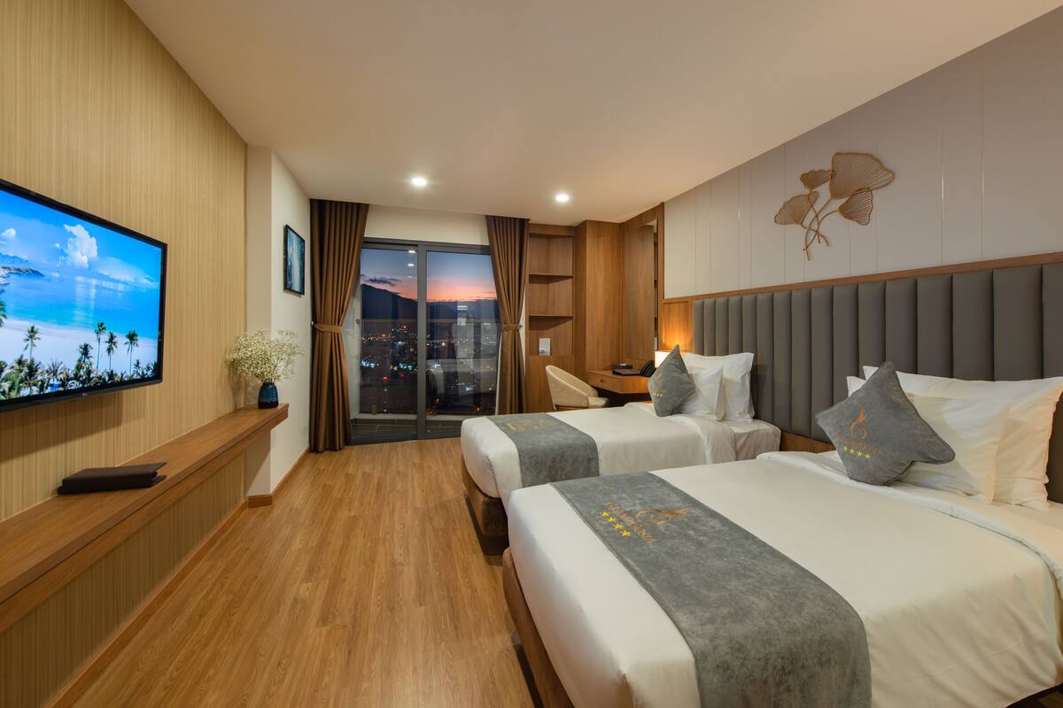 Hotelkamer met twee bedden, een televisie aan de muur, uitzicht op de stad en een houten vloer.