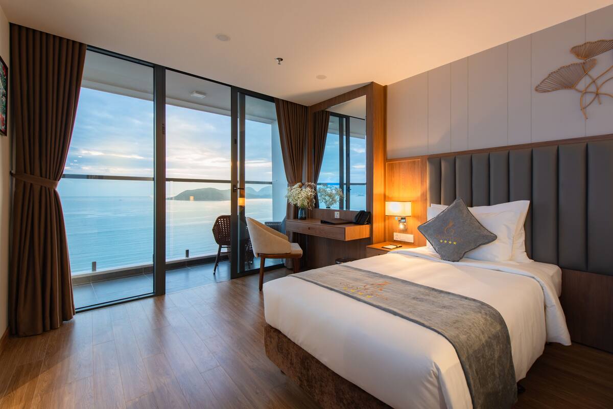 Een moderne hotelkamer met een groot bed, een bureau, een stoel en uitzicht op zee.