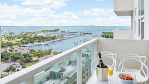 A balcony with a view of a marina, a bottle of champagne, and a glass of orange juice on a table. - Blue Accent Studio Suite | Bay & City Views (Miami)