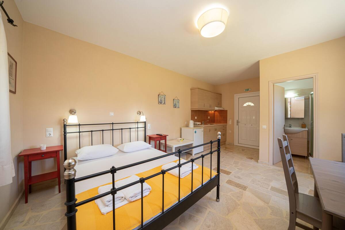 A hotel room with a bed, bedside tables, a desk, a chair, a bathroom, and a kitchen area.