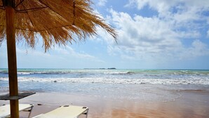 Una playa con una sombrilla de paja y una silla de descanso.