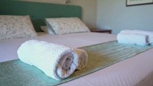 Una cama bien hecha con toallas blancas enrolladas, un cabecero verde azulado y una almohada estampada con motivos florales.