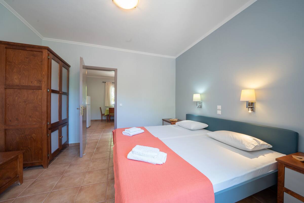 A hotel room with a bed, a wooden wardrobe, a nightstand, and a wall-mounted lamp.