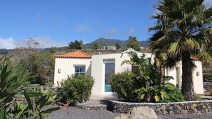 A small, single-story building with a tiled roof, surrounded by tropical plants and a stone wall. - Casa de las Estrellas (Los Llanos)