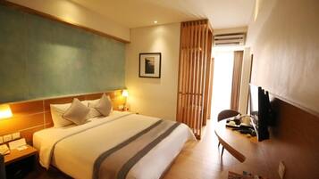 Habitación de hotel con cama, mesitas de noche, escritorio, silla, televisor y ventana con cortinas.