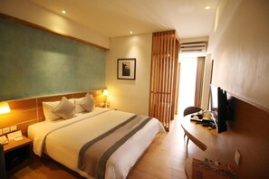 A hotel room with a bed, bedside tables, a desk, a chair, a television, and a window with curtains. - Liberta Hotel Jimbaran (Kedonganan)