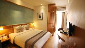A hotel room with a bed, bedside tables, a desk, a chair, a television, and a window with curtains. - Liberta Hotel Jimbaran (Kedonganan)