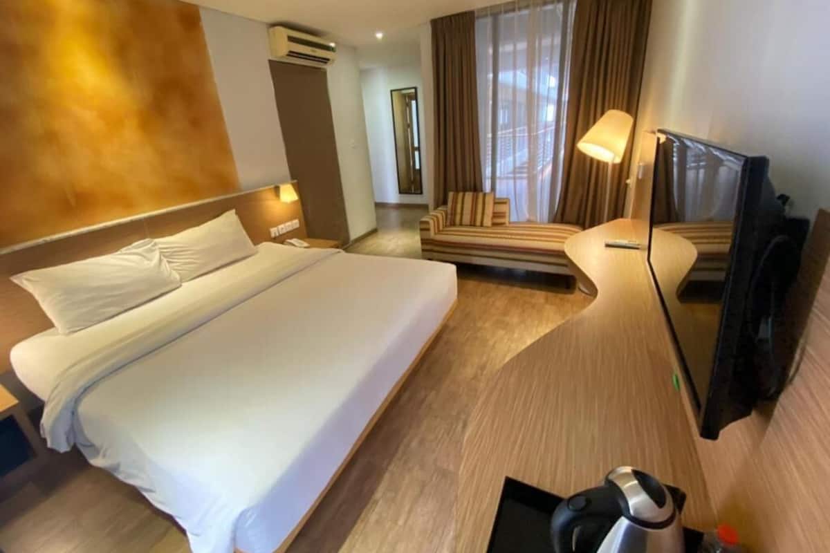Een hotelkamer met een groot bed, een bank, een televisie en een airconditioning.