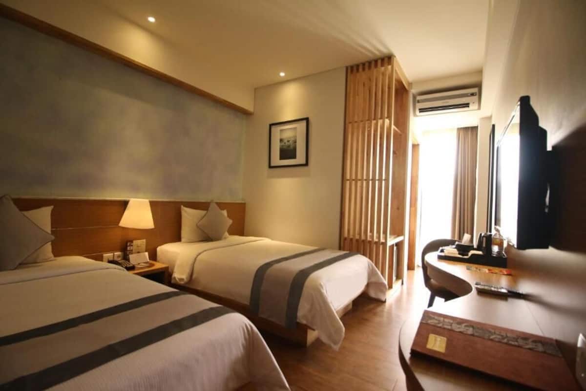 Een hotelkamer met twee bedden, een bureau, een stoel, een televisie en een foto aan de muur.