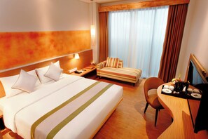 Habitación de hotel con una cama grande, un escritorio con silla, televisión y ventana con cortinas.