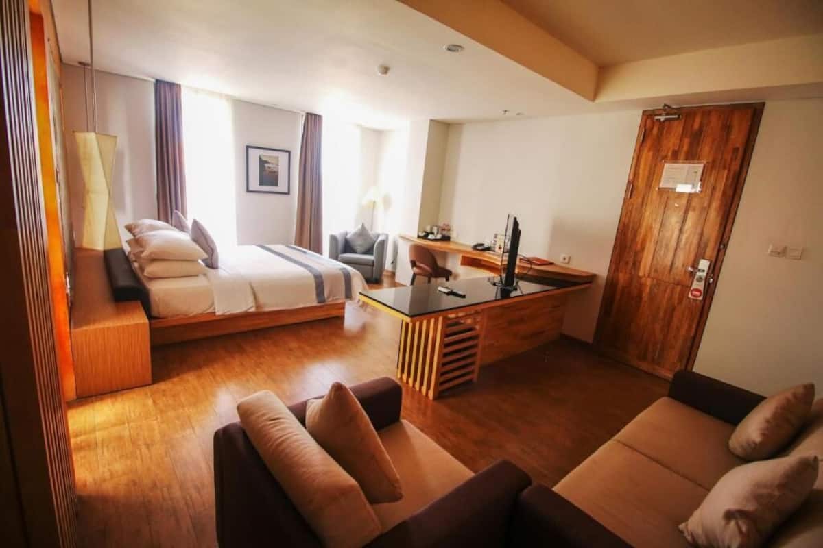 Een moderne hotelkamer met een bed, een bureau, een bank en een houten deur.