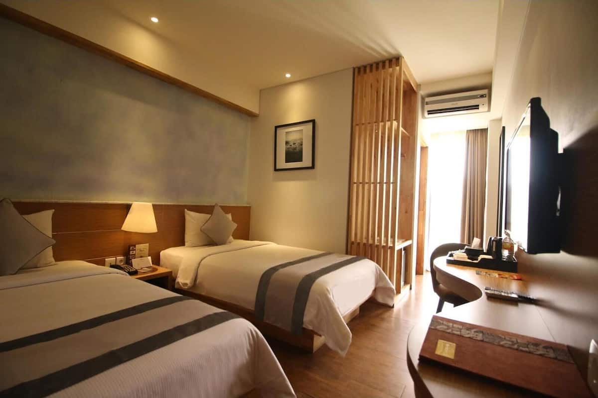 Een hotelkamer met twee bedden, een bureau met stoel, een televisie en een airconditioning.