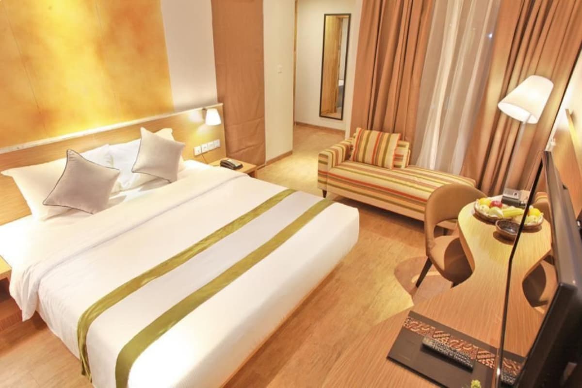 A hotel room with a large bed, a sofa, a small table with fruits, and a lamp.