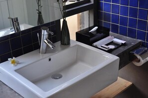 A bathroom with a white sink, a mirror, a vase with a flower, and a blue tiled wall. - Liberta Hotel Jimbaran (Kedonganan)