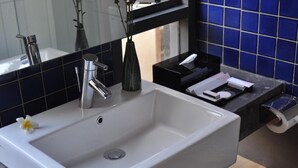A bathroom with a white sink, a mirror, a vase with a flower, and a blue tiled wall. - Liberta Hotel Jimbaran (Kedonganan)