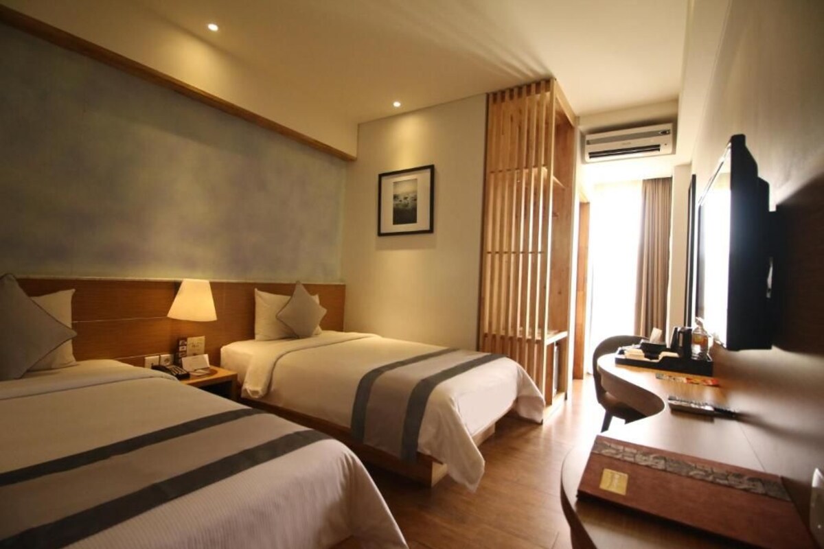 A hotel room with two beds, a desk, a chair, a TV, and a picture on the wall.