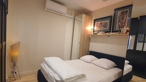 A bedroom with a bed, an air conditioning unit, a lamp, and framed artwork on the wall. - Jaures 2 bedrooms 7 minuts walking from Palais (Cannes)