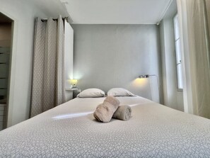 A hotel room with a bed, two pillows, a nightstand with a lamp, and a window with curtains.