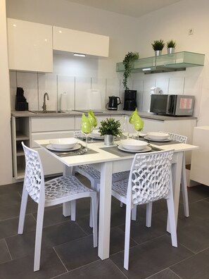 Une cuisine moderne avec des meubles blancs, une table à manger avec quatre chaises et un four à micro-ondes posé sur le plan de travail.