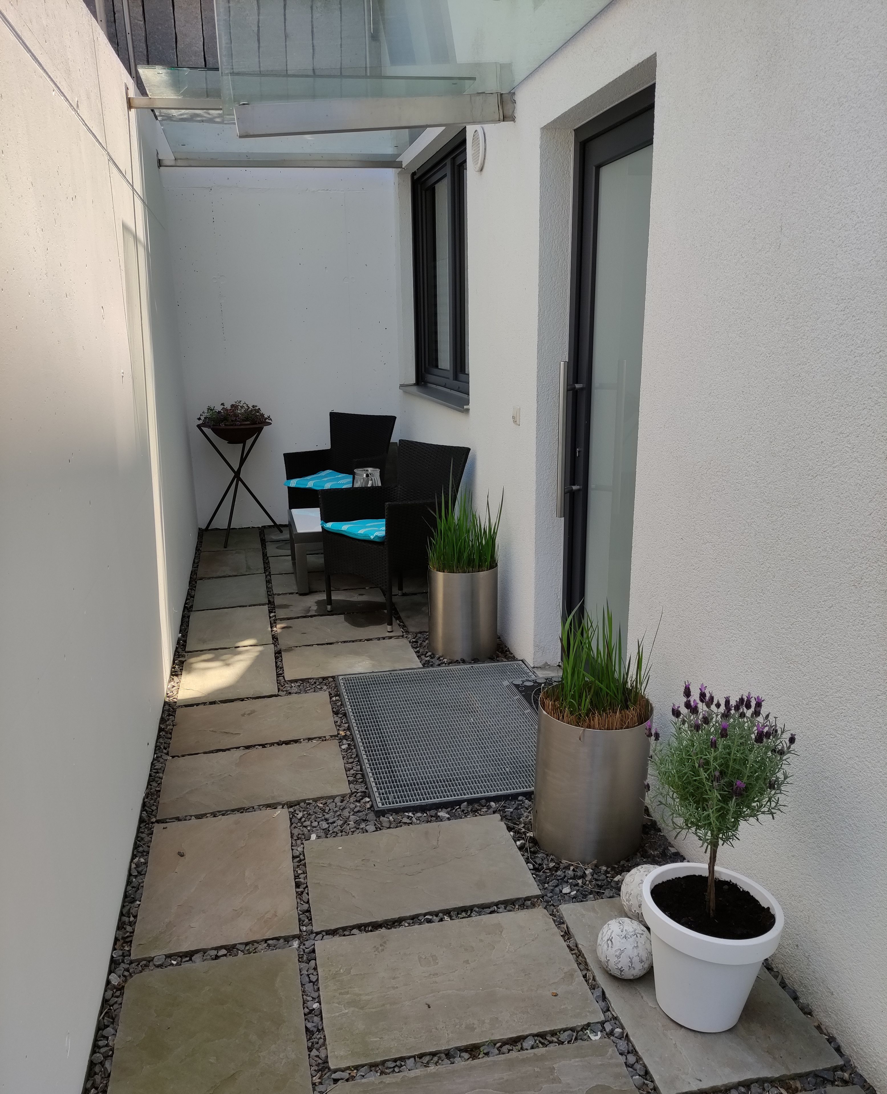 Eine schmale Außenpatio mit Sitzgelegenheit, Topfpflanzen und einem kleinen Tisch.