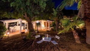 Un área de comedor al aire libre con una mesa y sillas, rodeada de árboles y una casa con porche.