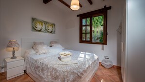 Un dormitorio con cama, mesita de noche, lámpara, ventana con vistas y un cuadro en la pared.