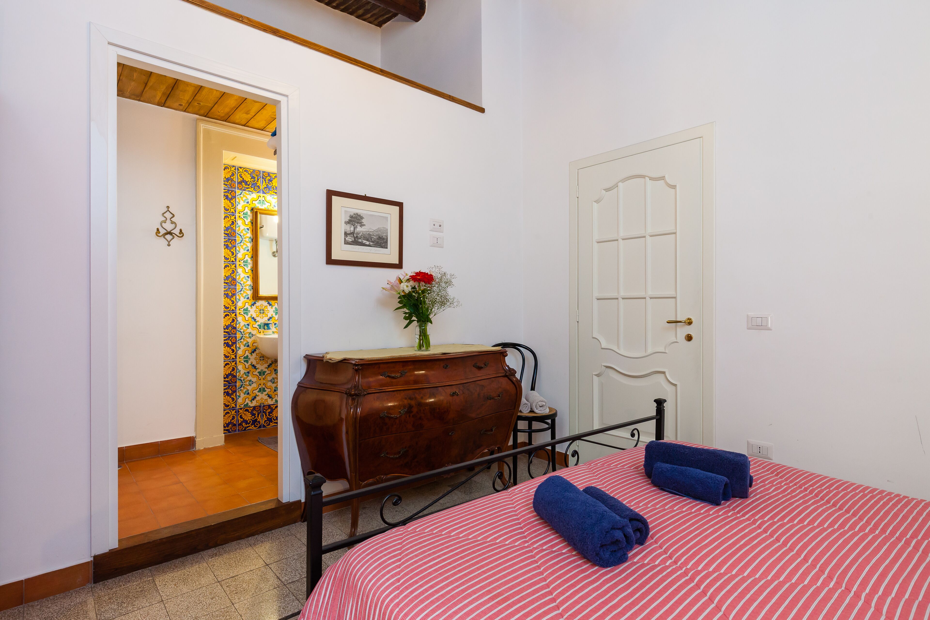 Une chambre à coucher avec un lit, une commode, une porte et une salle de bain visible à travers une porte ouverte.