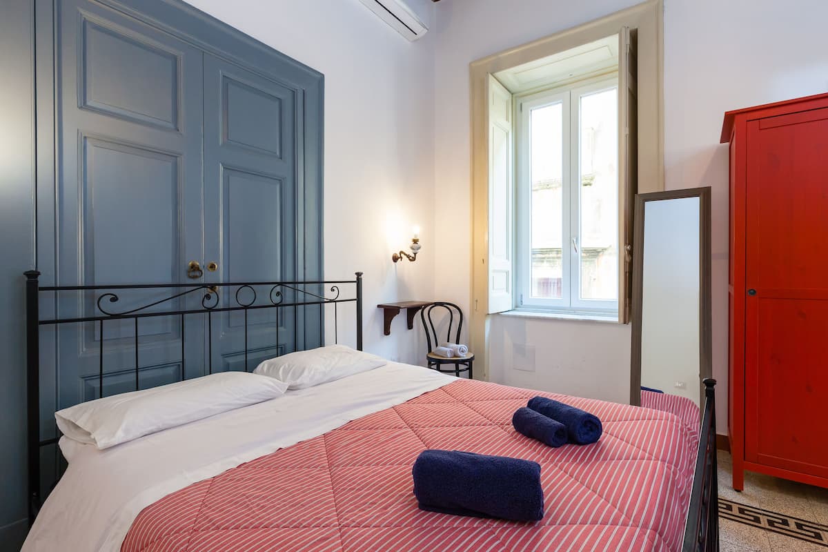 A bedroom with a bed, a window, a chair, and a wardrobe.
