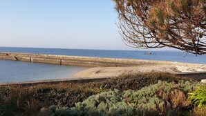 A coastal view with a concrete sea wall, sandy beach, and dense shrubbery. - Joli Studio Avec Grand Balcon vue mer (Concarneau)