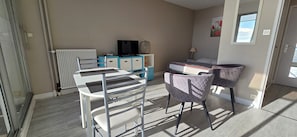 Quarto com cama, escrivaninha, cadeira, televisão e janela.