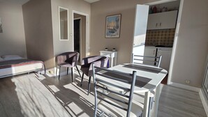 A bedroom with a bed, a chair, a table, and a kitchenette. - Joli Studio Avec Grand Balcon vue mer (Concarneau)